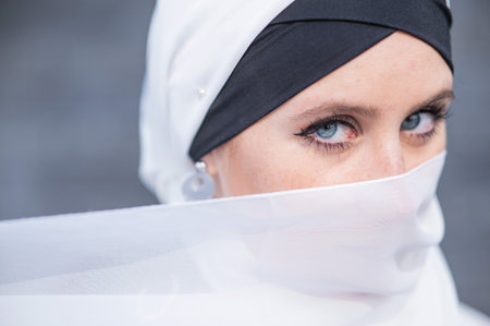 Portrait of a young blue-eyed woman in a hijab against a gray brick wall. Muslim woman with white scarf covering her face.の写真素材