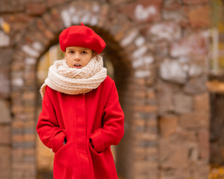 Caucasian girl in a red coat and beret is freezing on a walk in the autumn park.の写真素材