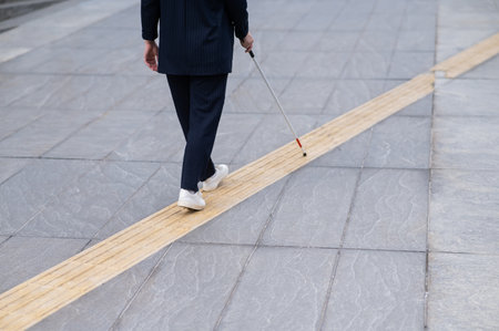 Close-up of the legs of a blind businesswoman walking along a tactile tile with a cane.の写真素材