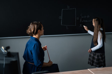 Caucasian little girl answers the question of the female teacher at the blackboard.