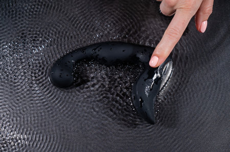 A woman holds a black prostate stimulator that vibrates and creates ripples on the surface of the water against a black background.の写真素材