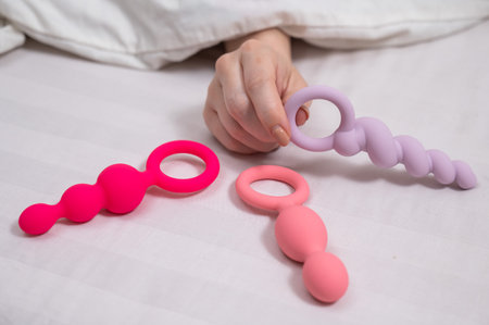A woman chooses anal beads from a set while lying in bed.の写真素材