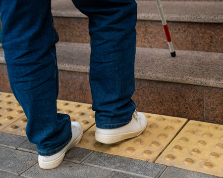 Close-up of female foot, walking stick and tactile tiles. Blind woman climbing stairs using a cane.の写真素材