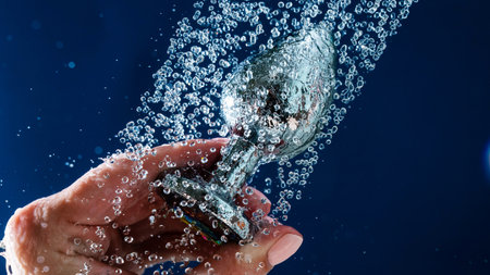 Woman washing silver anal plug under shower on blue background.の写真素材