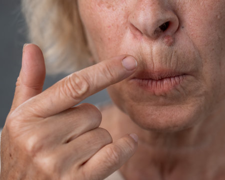 Unhappy elderly woman pointing at wrinkles around her lips.の写真素材