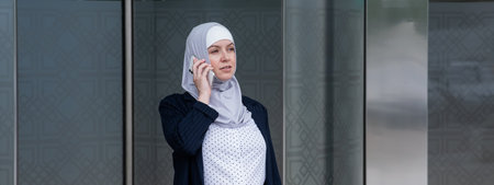 Business woman in hijab and suit talking on smartphone while leaving the business center.