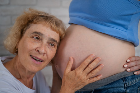 An elderly woman leans against the belly of her pregnant daughter. Close-up.の写真素材