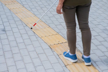 Close-up of the legs of an elderly blind woman with a cane at a tactile tile.の写真素材