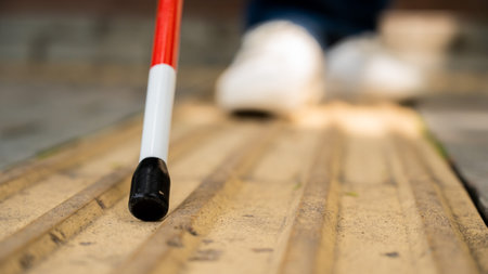 A blind woman walks on the street on tactile yellow tiles. Focus on the tactile cane.の写真素材