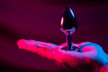 Woman holding metal anal plug in neon pink purple light.の写真素材