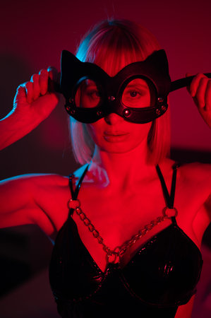 Blonde woman wearing a leather mask in red blue neon light and holding a steel butt plug.の写真素材