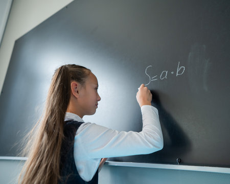 The schoolgirl answers at the lesson. Caucasian girl writes a formula on a blackboard.の写真素材