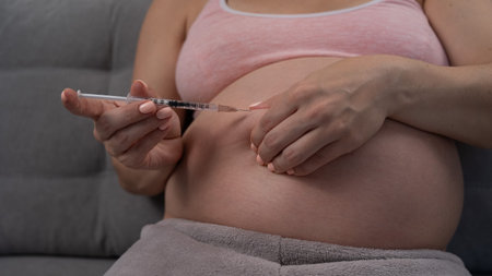 A pregnant woman puts an injection of insulin while sitting on the couch. Close up of the belly.の写真素材