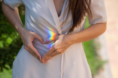 Faceless woman catching rainbow ray with her hands outdoors. Girl makes a heart with her handsの写真素材