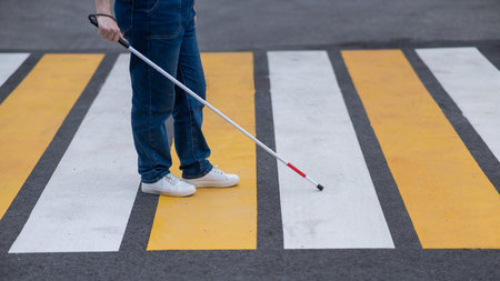 Close-up of the legs of a blind woman crossing the road at a crosswalk with a cane.の写真素材