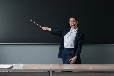 Red-haired caucasian woman in a trouser suit. Smiling female teacher with a pointer at the...