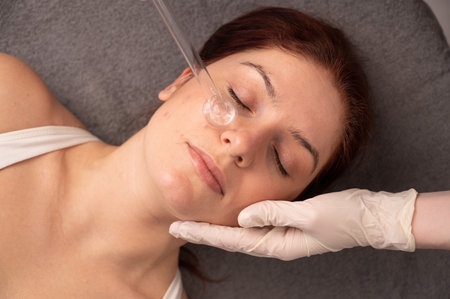 The doctor uses the darsonval apparatus against acne on the face of a female patient
