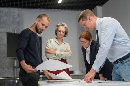 Four business people review and discuss blueprints. Designers engineers at a meetingの写真素材