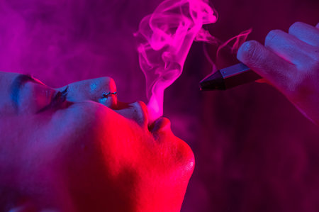 Portrait asian woman smokes vape in neon light