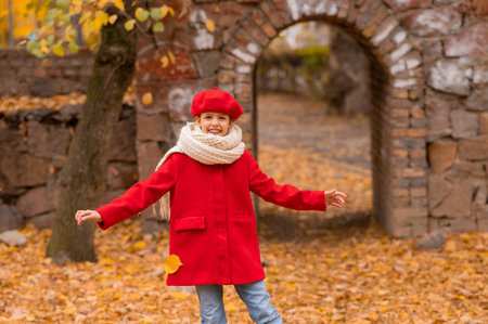 Happy caucasian girl in a red coat and beret walks in the park in autumnの写真素材