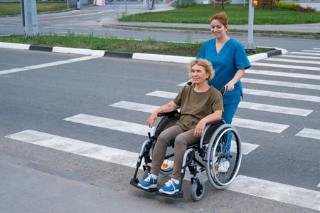 Red-haired nurse pushing an elderly woman in a wheelchair across the road