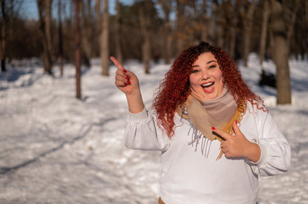 A chubby red-haired woman in a white sweatshirt. Girl fooling around in the park in winter