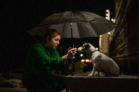Red-haired woman and dog jack russell terrier under an umbrella in the dark