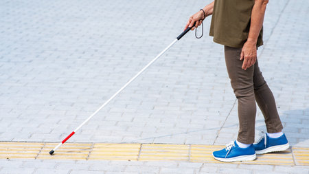 Close-up of the legs of an elderly blind woman with a cane at a tactile tileの写真素材
