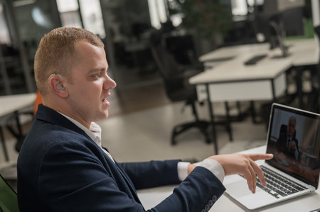 Caucasian man with hearing aid at online meeting on laptopの写真素材