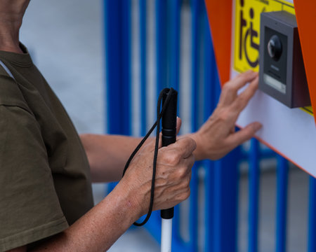 Close-up of the hands of a blind elderly woman reading a text in braille. Button for calling help for people with disabilitiesの写真素材