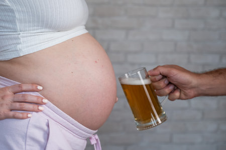 A man clinks a bottle of beer with a pregnant womans bellyの写真素材