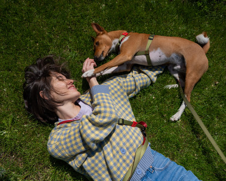 Top view of beautiful young woman and african basenji dog lying on green grassの写真素材