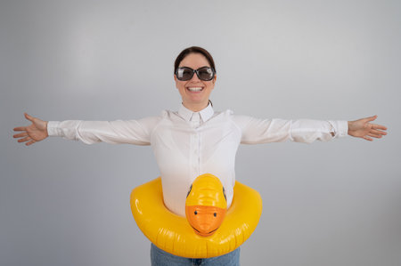 Caucasian woman in a white shirt dreaming of a vacation and wearing sunglasses and an inflatable duckの写真素材