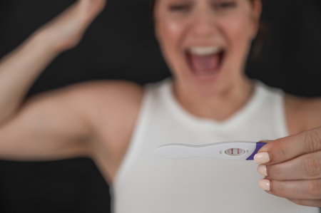 Blurred portrait of happy caucasian woman holding positive express pregnancy test on black backgroundの写真素材