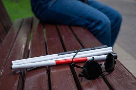 Sunglasses and a folding cane for the blind on a benchの写真素材