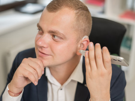 Caucasian man with a hearing aid talking on the phone on speakerphoneの写真素材