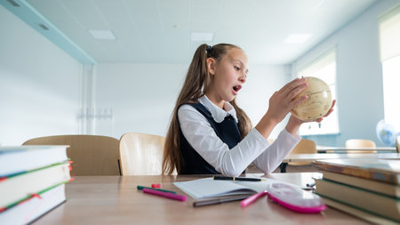 Caucasian schoolgirl sits at her desk at school and studies the globe