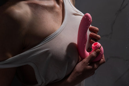 A woman in a white tank top stands in the shower and holds a curved pink sex toyの写真素材