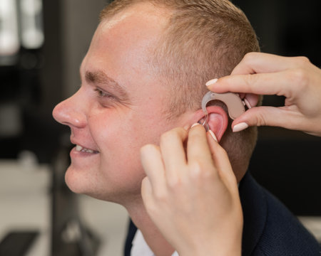 Woman putting hearing aid on Caucasian man