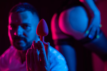 Bearded caucasian man holding an anal plug. Close-up of female buttocks in underwear. Sexual preferences of the coupleの写真素材