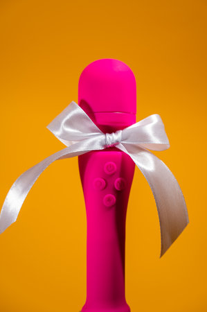 Pink vibrator with a white bow on an orange background. Womens gift