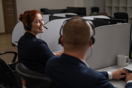 Two friendly call center employees answer customers by phone. Man and woman woman talking on a headset in the officeの写真素材