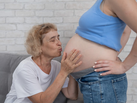 An elderly woman leans against the belly of her pregnant daughter. Close-upの写真素材
