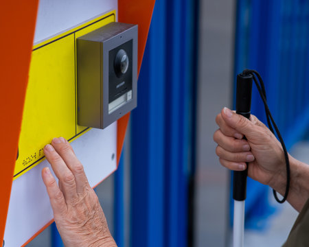 Close-up of the hands of a blind elderly woman reading a text in braille. Button for calling help...