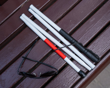 Sunglasses and a folding cane for the blind on a bench