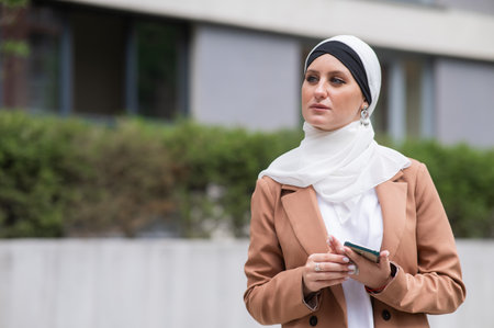 Young woman in hijab using smartphone outdoorsの写真素材
