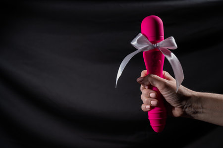 Woman holding pink vibrator with white bow on black background. Copy spaceの写真素材