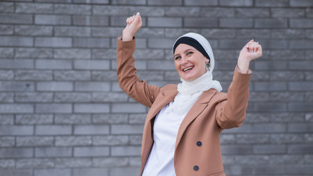 Portrait of a young blue-eyed woman in a hijab against a gray brick wall. Joyful Muslim womanの写真素材