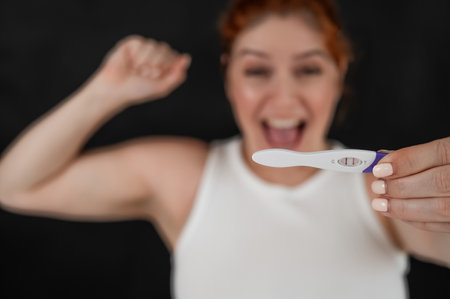Blurred portrait of happy caucasian woman holding positive express pregnancy test on black backgroundの写真素材