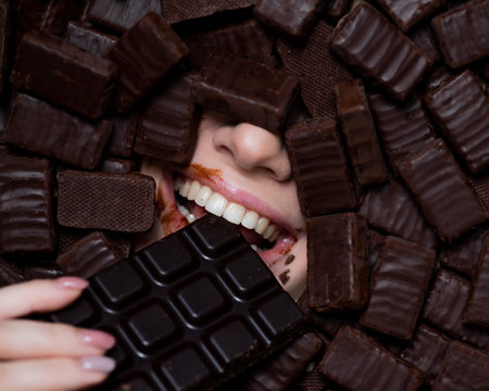 The face of a caucasian woman surrounded by chocolates. The girl eats a bar of chocolateの写真素材